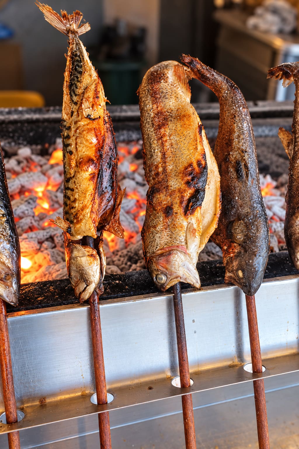 Steckerlfische stecken senkrecht auf Holzspießen über der Glut im Grill