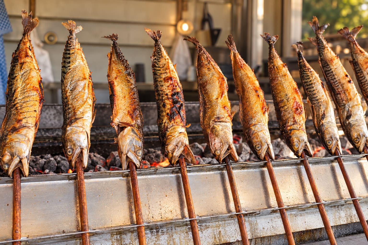 Goldbraun gegrillte Steckerlfische in einer Reihe am Grill im Abendlicht
